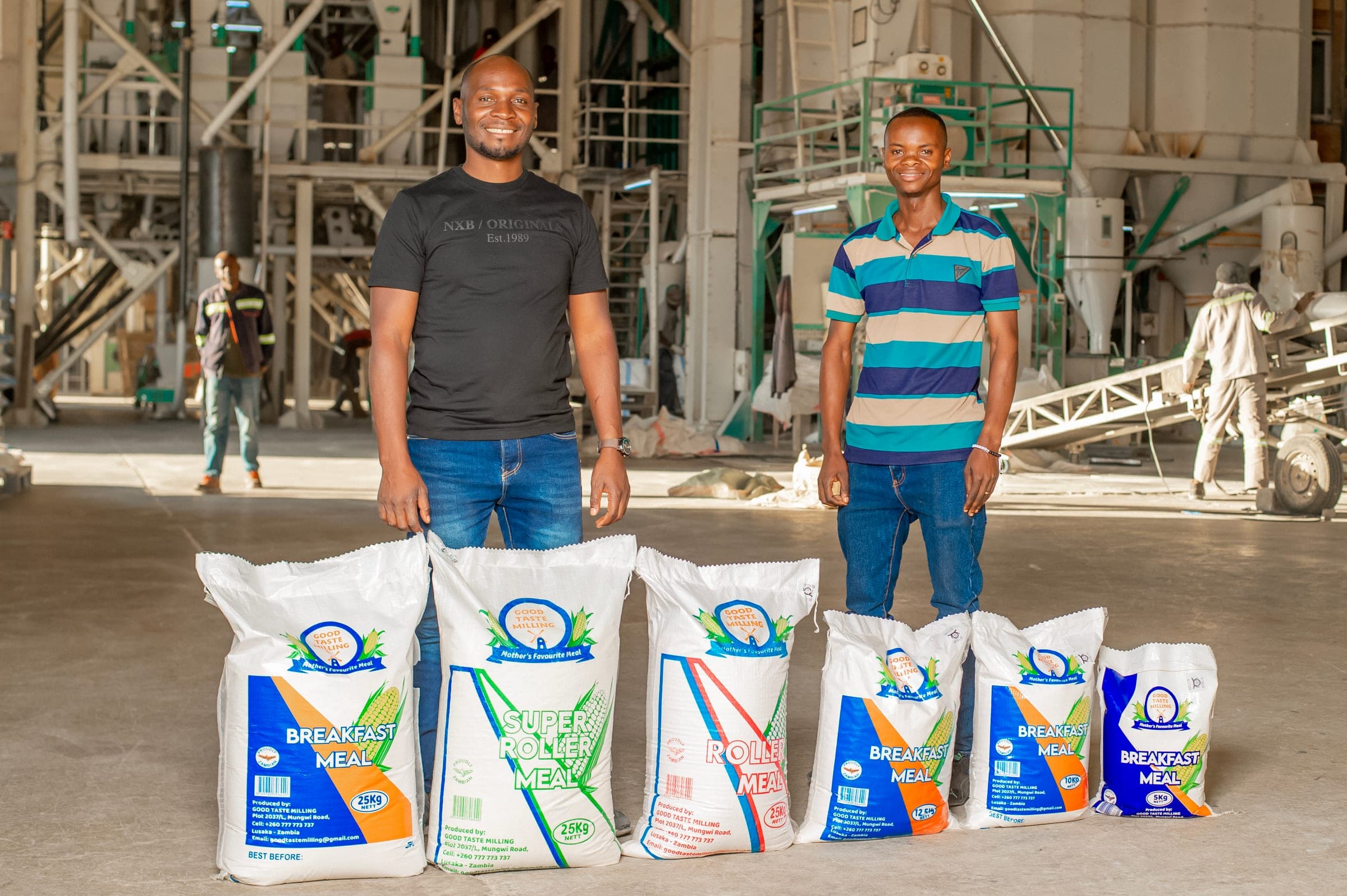 Two men standing behind the range of Good Taste Milling meal sacks on the mill floor